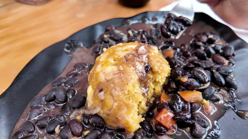 A bolón de verde, a green plantain ball, on a plate of bean menestra