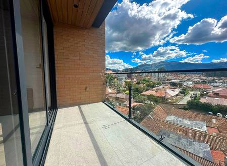 Balcony with gray tile flooring, brick wall, black glass railing, overlooking Cuenca cityscape with mountains and blue sky.