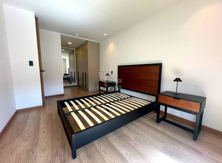 Bedroom with black metal bed frame, wooden headboard, nightstands with lamps, wood-look flooring, and open door to ensuite bathroom.