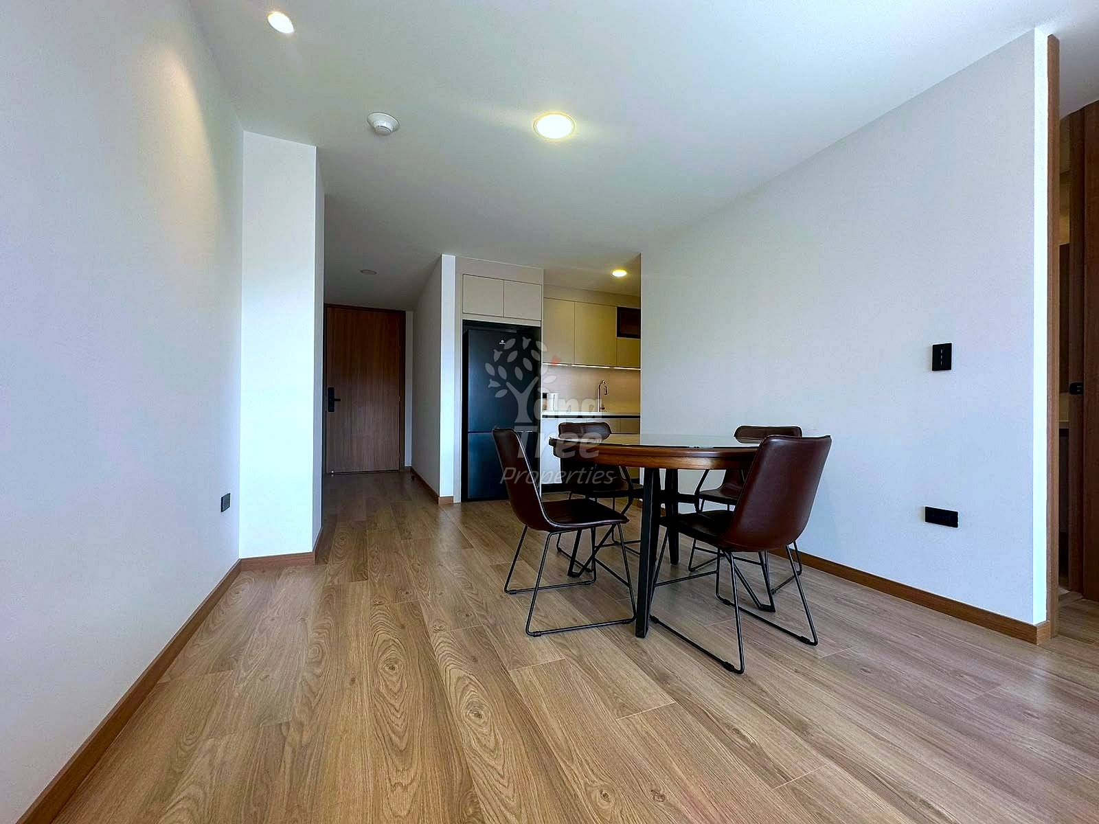 Open-plan living and dining area with wood flooring, dining table with brown chairs, kitchen with appliances visible, recessed lighting, white walls, and brown wood doors.
