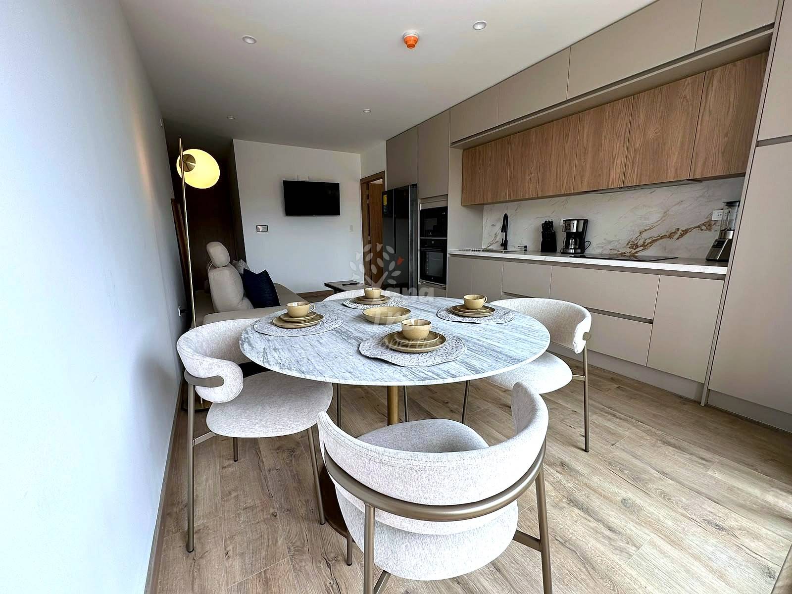 Open-plan dining and kitchen area with round marble table, four upholstered chairs, wood cabinetry, and recessed lighting.