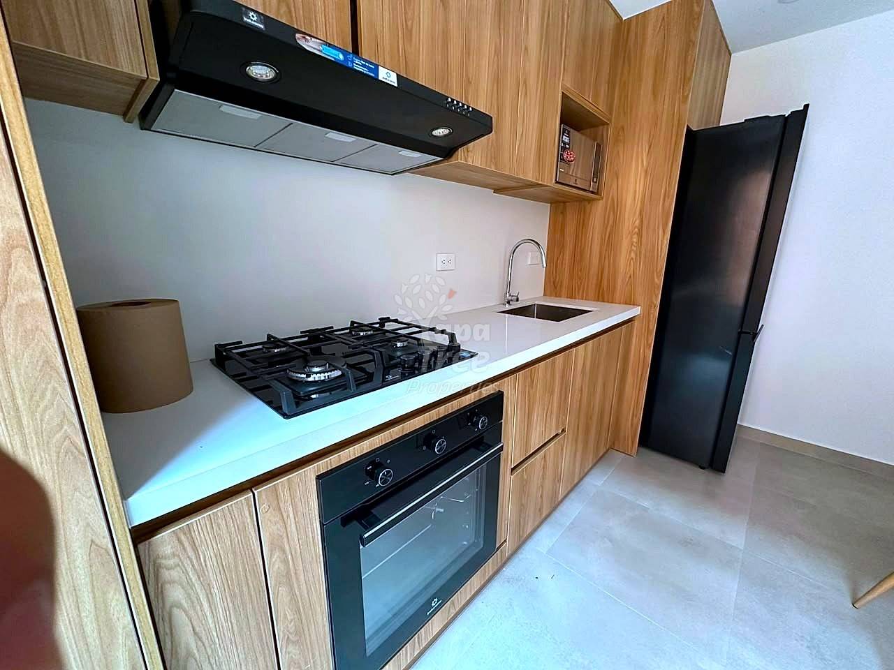Modern cocina with wood cabinetry, white countertop, gas cooktop, built-in oven, black range hood, and stainless steel sink with chrome faucet.