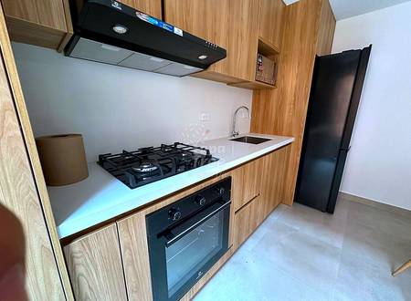 Modern cocina with wood cabinetry, white countertop, gas cooktop, built-in oven, black range hood, and stainless steel sink with chrome faucet.