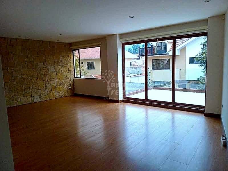 Living room with wood laminate flooring, stone accent wall on left, large sliding glass doors opening to balcony with city views, recessed ceiling lights.