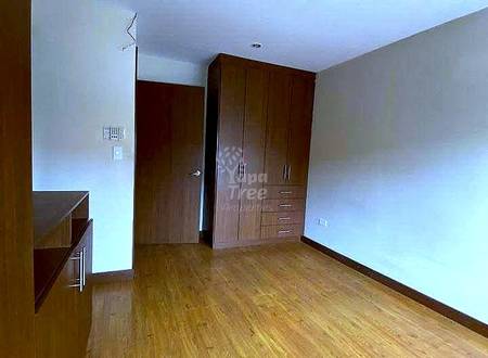 Bedroom with wooden flooring, dark wood wardrobe cabinets, white walls, recessed ceiling light, and built-in shelving on left side.