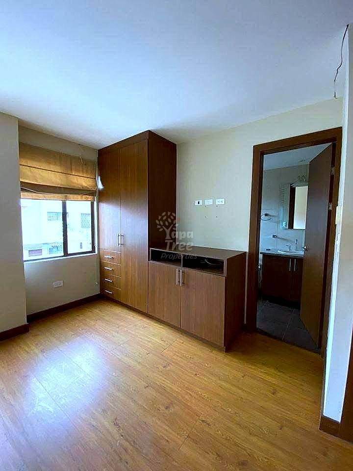 Bedroom with wood flooring, built-in dark wood wardrobes, vanity desk, window with wooden blinds, and doorway to ensuite bathroom