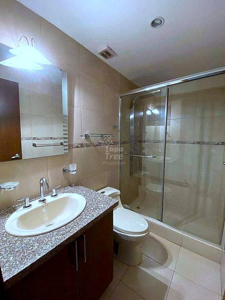 Bathroom with cream tile walls, round sink on speckled granite counter, wooden cabinet, glass shower enclosure, and white toilet.