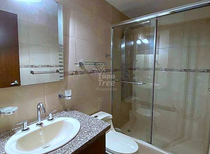 Bathroom with cream tile walls, round sink on speckled granite counter, wooden cabinet, glass shower enclosure, and white toilet.