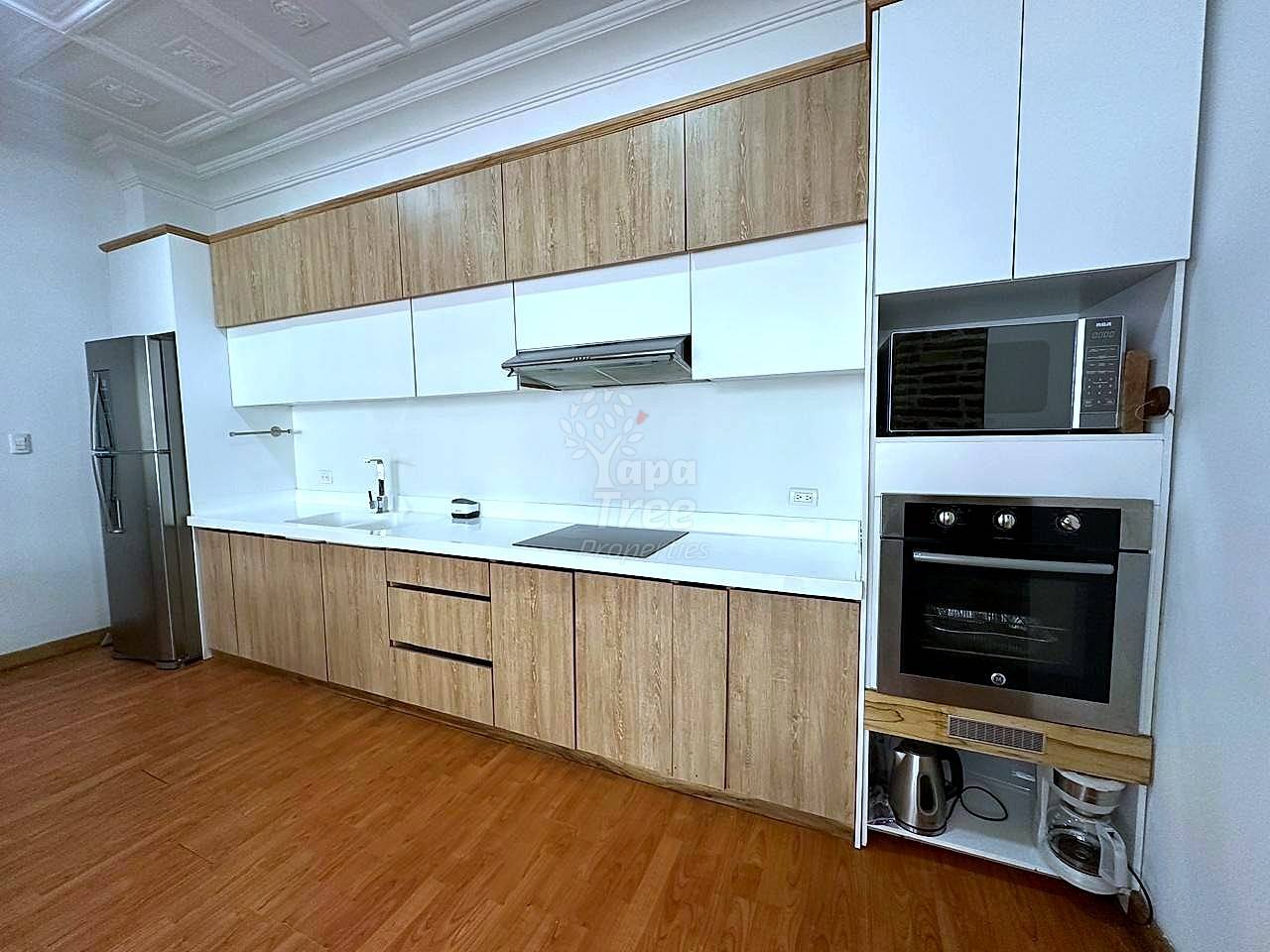 Modern cocina with wood and white cabinetry, white quartz countertop, black electric oven, microwave, stainless steel refrigerator, and wood flooring.