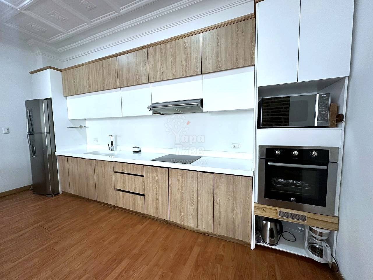 Modern cocina with wood and white cabinetry, white quartz countertop, black electric oven, microwave, stainless steel refrigerator, and wood flooring.