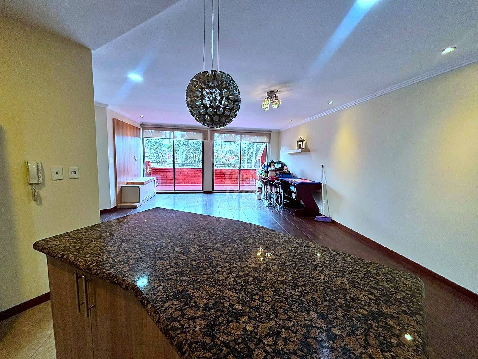 Open kitchen and living area with granite island countertop, recessed lighting, yellow walls, and glass doors opening to a balcony with red railings.