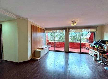 Open living room with dark wood flooring, cream walls, large sliding glass doors overlooking red brick terrace, and built-in wooden storage bench.