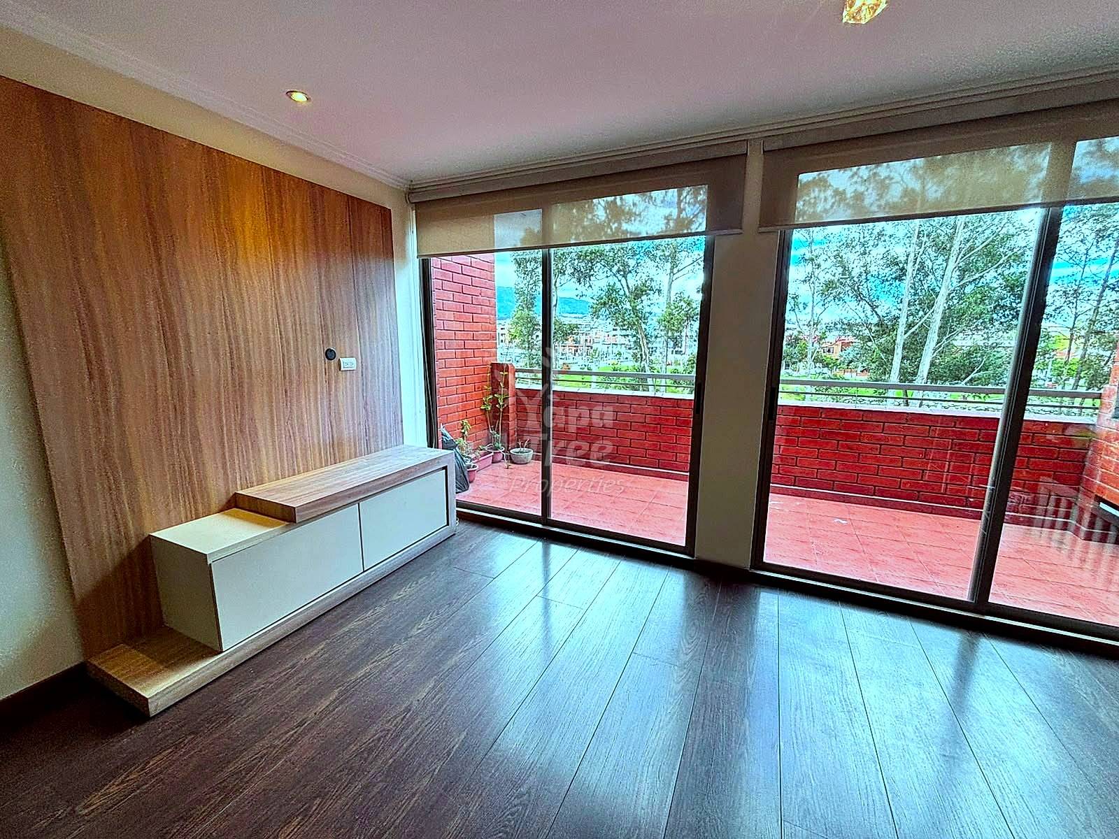 Bedroom with wood flooring, white built-in bench, wood-paneled wall, and sliding glass doors opening to red brick terrace with city views.