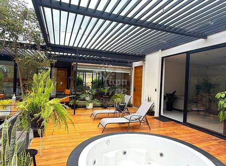 Outdoor patio with wooden deck, built-in hot tub, lounge chairs, potted plants, and slatted metal pergola overhead.