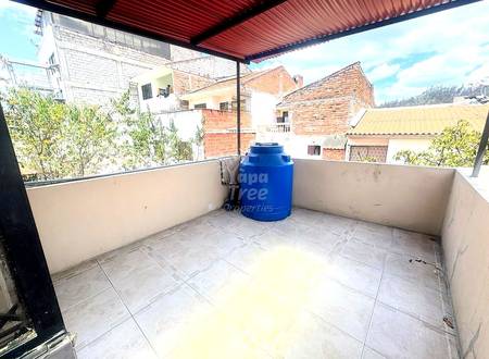 Rooftop terrace with gray tile flooring, blue water storage tank, corrugated metal roof, and surrounding brick buildings in daylight.