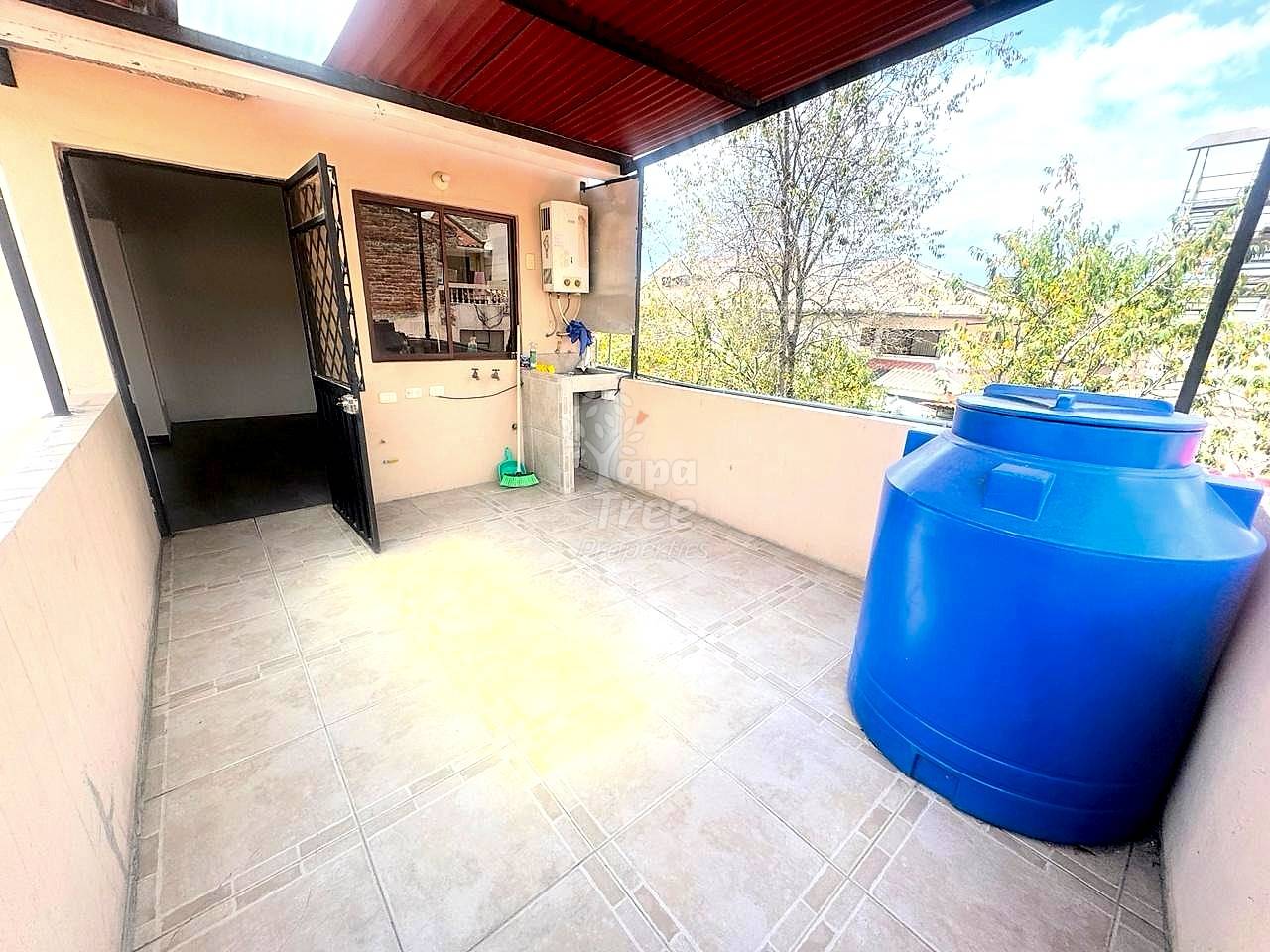 Rooftop terrace with tile flooring, sink basin, water heater, open black door, and two large blue storage tanks with city view.