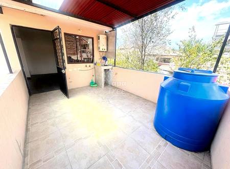 Rooftop terrace with tile flooring, sink basin, water heater, open black door, and two large blue storage tanks with city view.