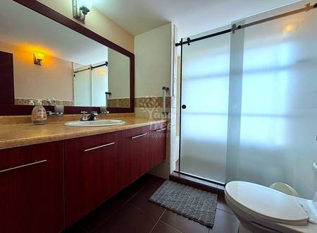 Modern bathroom with dark wood vanity, marble countertop, large mirror with dark frame, glass shower enclosure with sliding door, and white soaking tub.
