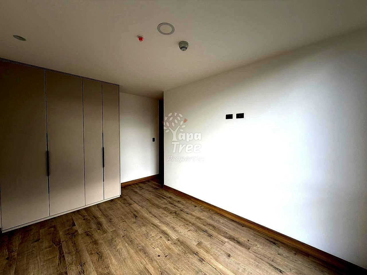Bedroom with white paneled wardrobe, laminate wood flooring, white walls, ceiling with smoke detector and light fixture