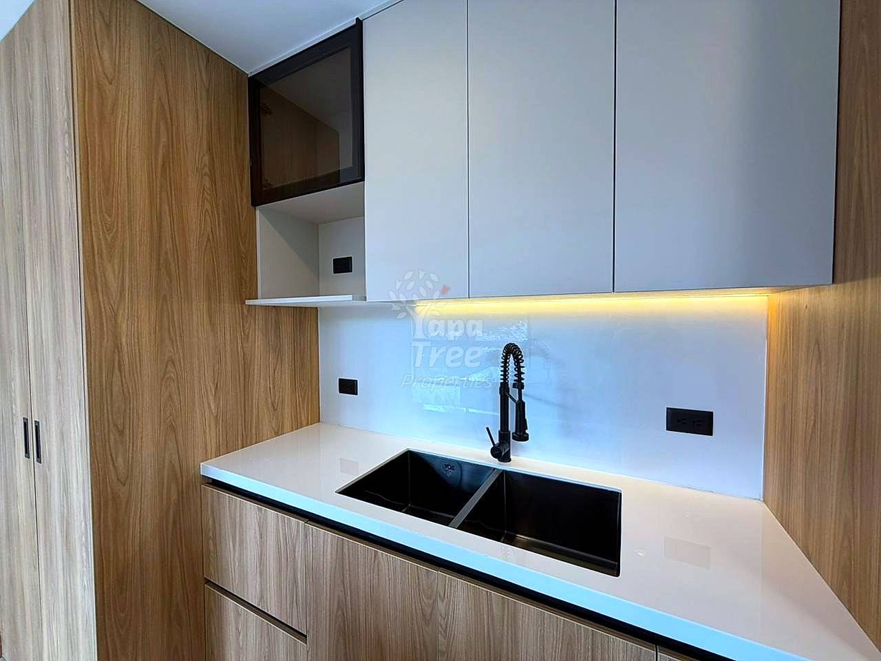 Modern cocina with wood-grain cabinetry, white countertop, double black sink, white tile backsplash, and warm under-cabinet lighting.