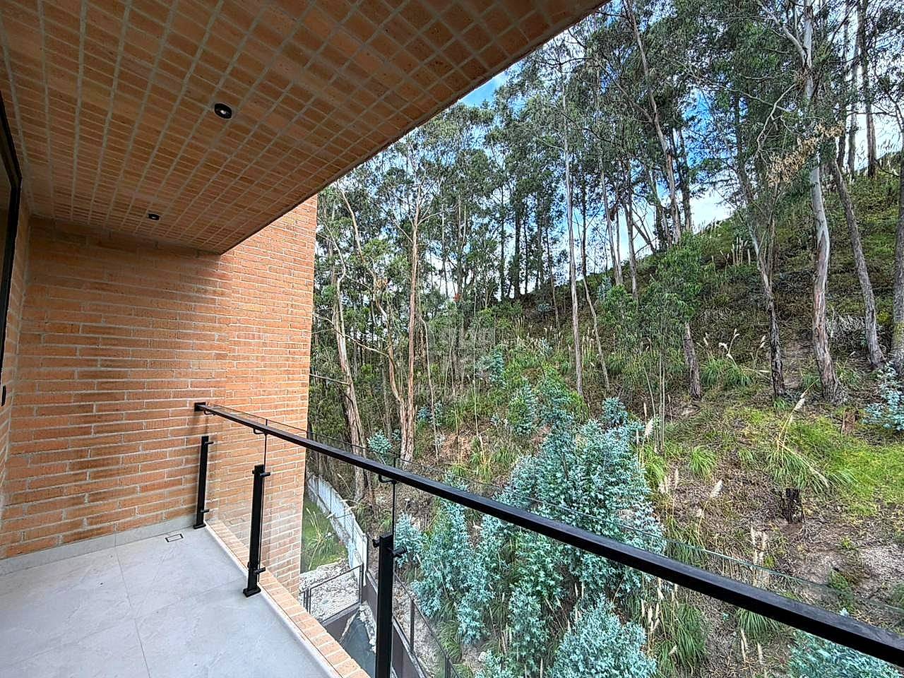 Covered terrace with red brick wall, black metal railing, and view of eucalyptus forest and hillside vegetation.