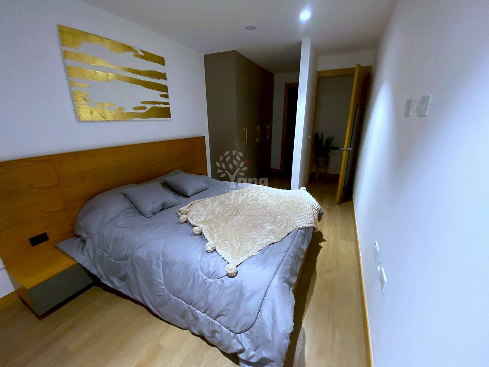 Bedroom with wood-framed bed, gray bedding, wooden headboard, built-in wardrobe, and laminate flooring under bright ceiling lighting.