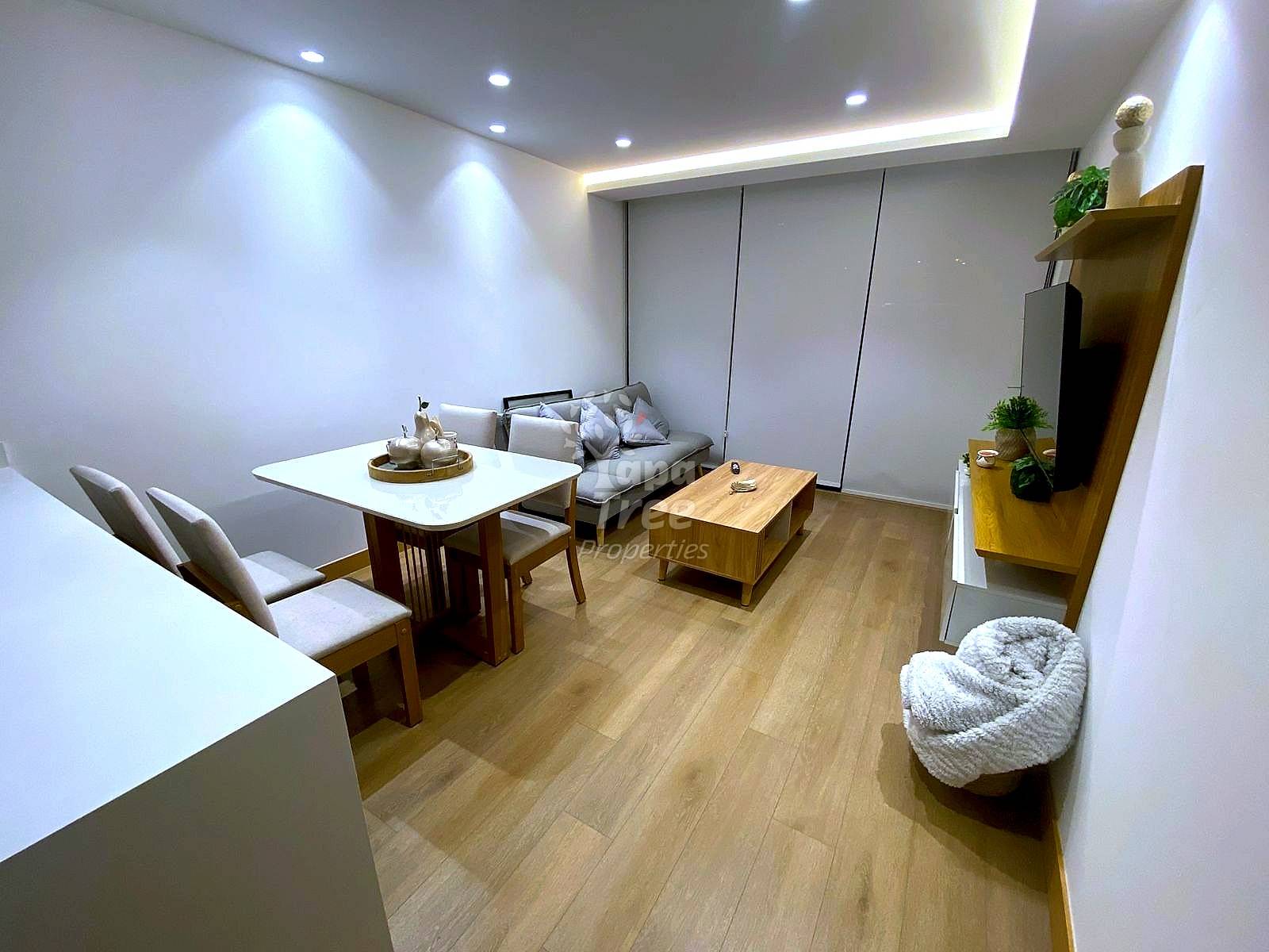 Modern suite interior with wood flooring, dining table with chairs, gray sofa, coffee table, and recessed ceiling lights throughout.
