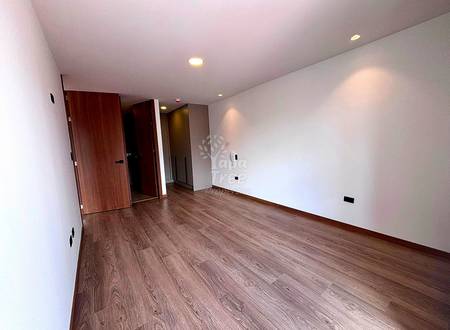Empty bedroom with wood-grain laminate flooring, white walls, recessed ceiling lights, and wooden entry door with white frame.