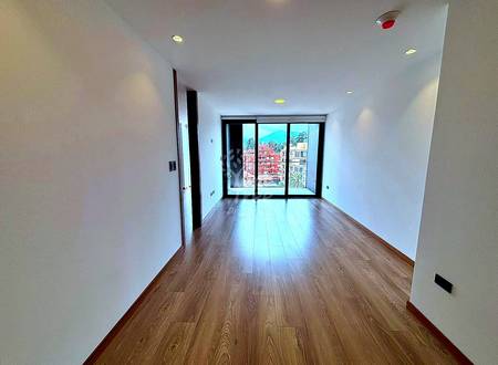 Empty room with wooden flooring, white walls, recessed ceiling lights, and glass sliding doors overlooking Cuenca cityscape with red brick buildings.
