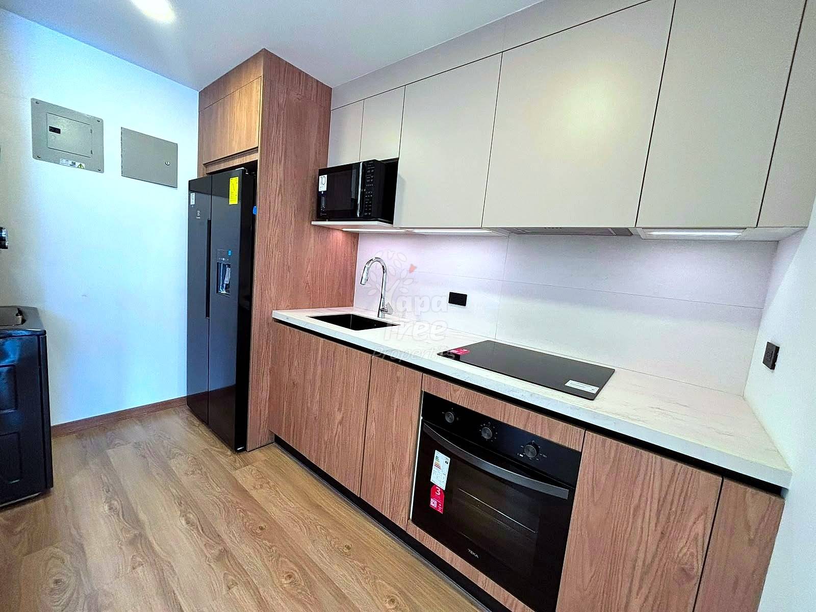 Modern kitchen with wood-grain cabinetry, white countertop, black appliances, microwave, cooktop, sink, and wood flooring throughout the room.