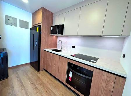 Modern kitchen with wood-grain cabinetry, white countertop, black appliances, microwave, cooktop, sink, and wood flooring throughout the room.