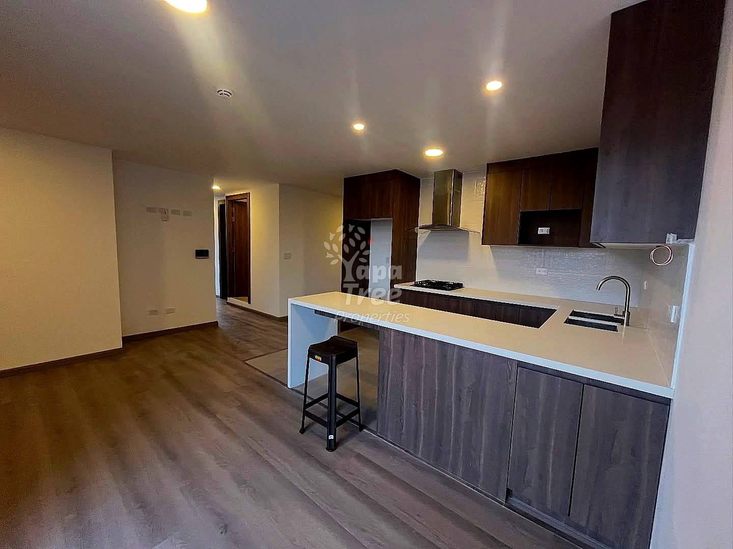 Open-concept departamento with dark wood cabinetry, white quartz island countertop, gas cooktop, and recessed ceiling lights throughout.