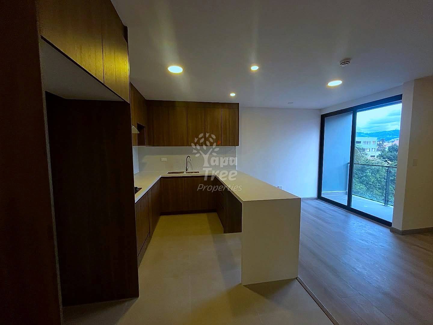 Modern kitchen with dark wood cabinetry, beige countertop island, recessed lighting, and sliding glass door opening to balcony with mountain views.