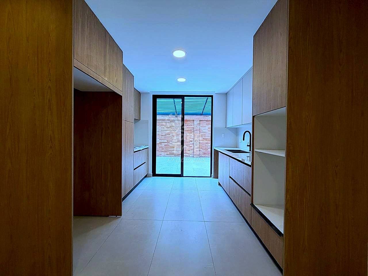Modern kitchen with wood cabinetry on both sides, tile flooring, recessed lighting, and glass doors opening to brick patio.