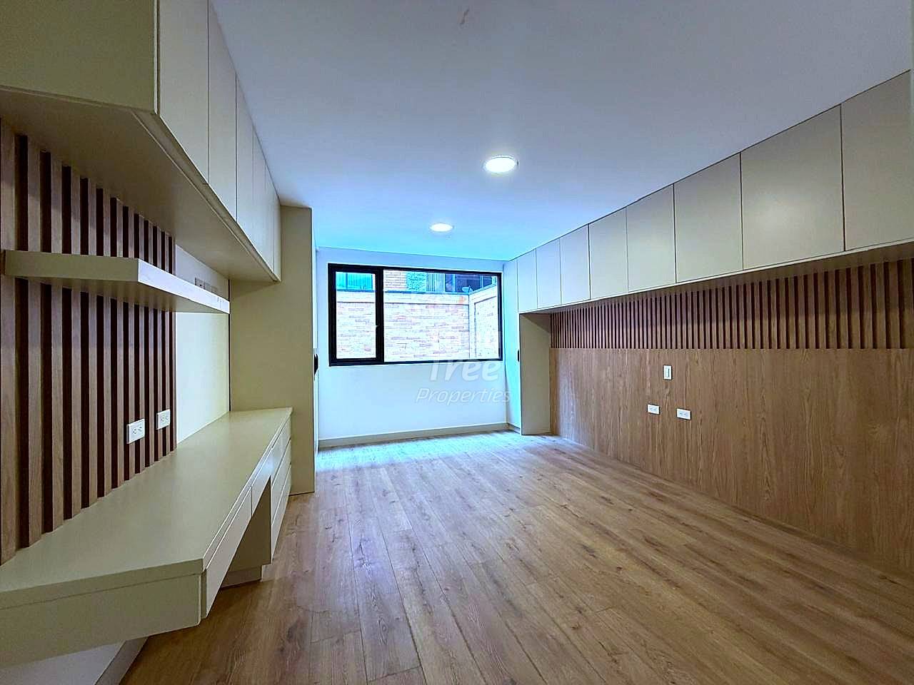 Empty room with wood laminate flooring, built-in white and brown cabinetry with vertical slat details, recessed ceiling lights, and window with brick exterior view.