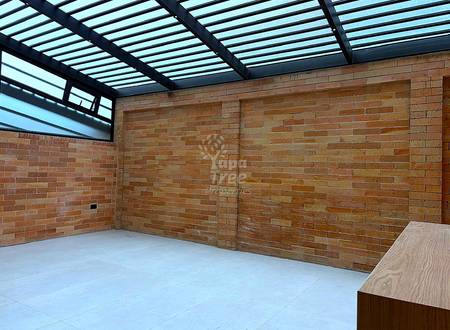 Empty room with exposed red brick walls, light gray tile floor, black metal frame skylight roof, and wooden counter edge visible.