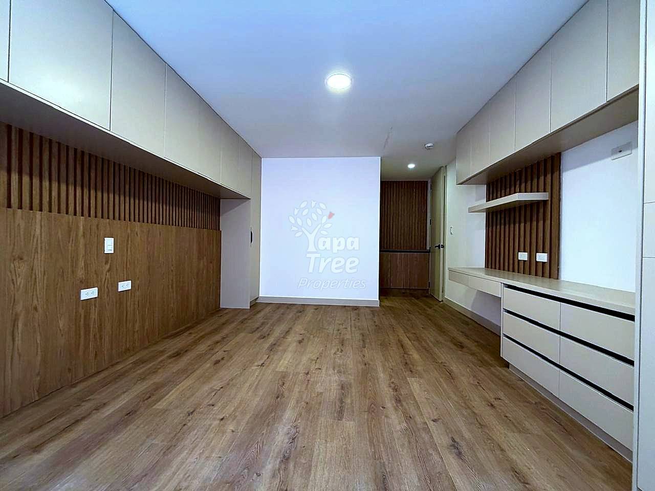 Empty departamento interior with wood-look laminate flooring, white ceiling with recessed lighting, cream and wood wall paneling, and built-in storage units.
