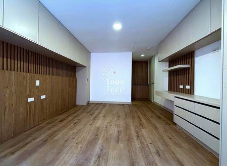 Empty departamento interior with wood-look laminate flooring, white ceiling with recessed lighting, cream and wood wall paneling, and built-in storage units.