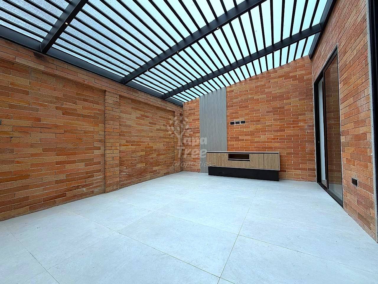 Empty interior room with red brick walls, polished concrete floor, metal-framed skylight roof, and built-in storage unit with wood and black finish