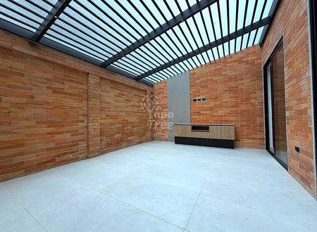 Empty interior room with red brick walls, polished concrete floor, metal-framed skylight roof, and built-in storage unit with wood and black finish