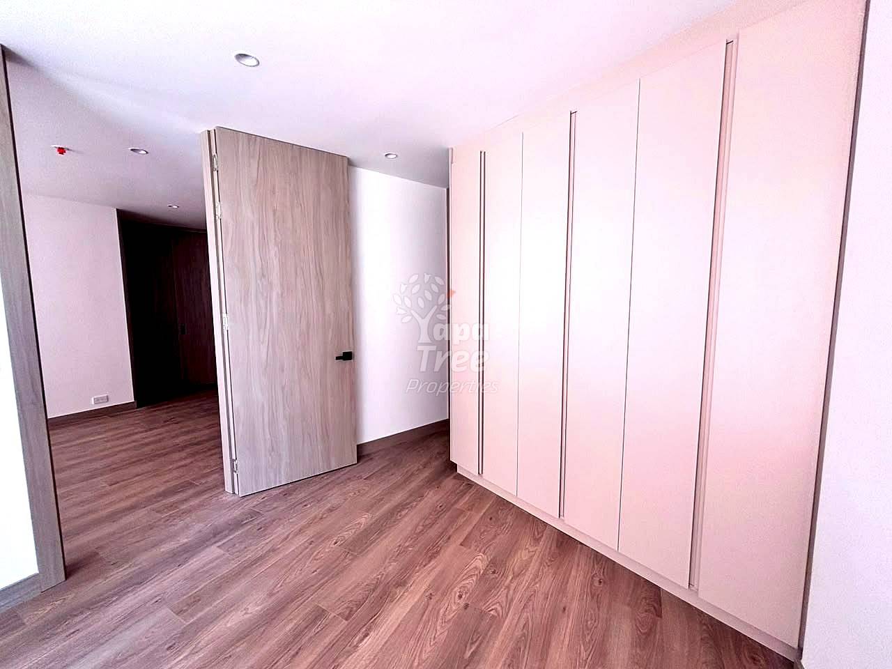 Bedroom with wooden laminate flooring, pink wardrobe cabinets with metal handles, and recessed ceiling lights.