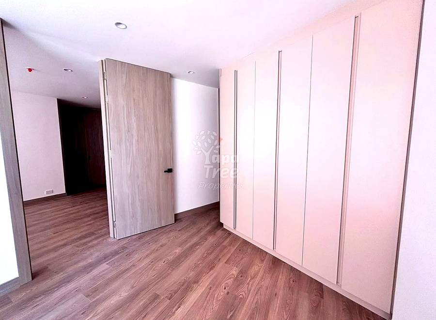 Dormitorio con piso laminado tipo madera, armarios rosados con tiradores metálicos, y luces embutidas en el techo.