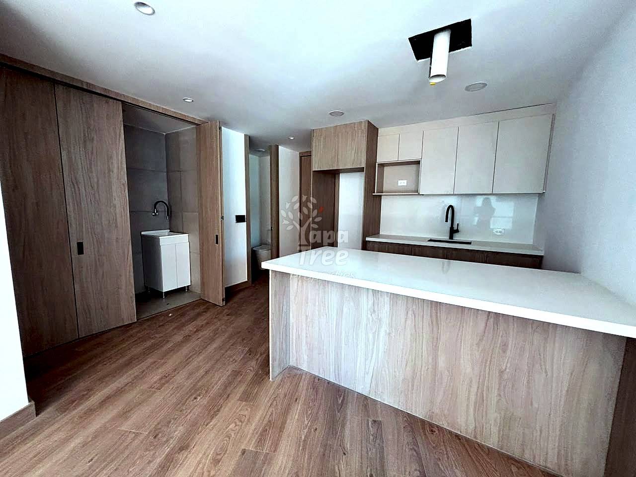 Cocina abierta con encimeras de cuarzo blanco, gabinetes de madera clara, isla con asientos y piso tipo madera.