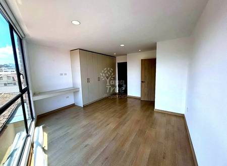 Bedroom with wood laminate flooring, built-in wardrobe with beige doors, desk area, wooden door, recessed ceiling lights, and large windows with city view.