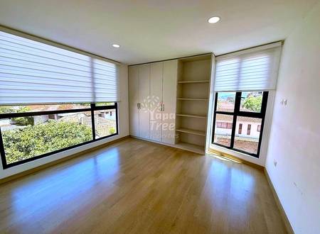 Bedroom with wooden floor, built-in wardrobe and shelving unit, two windows with roller blinds showing city views, recessed ceiling lights.