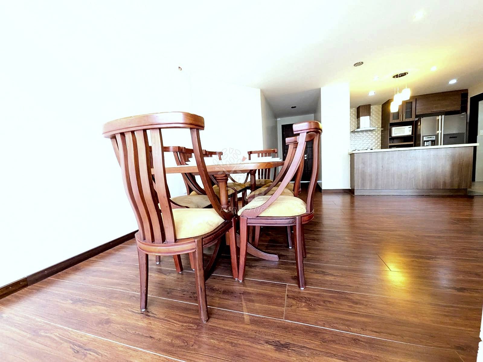 Open dining and kitchen area with wooden dining table, red chairs with cream cushions, hardwood flooring, and recessed lighting overhead.
