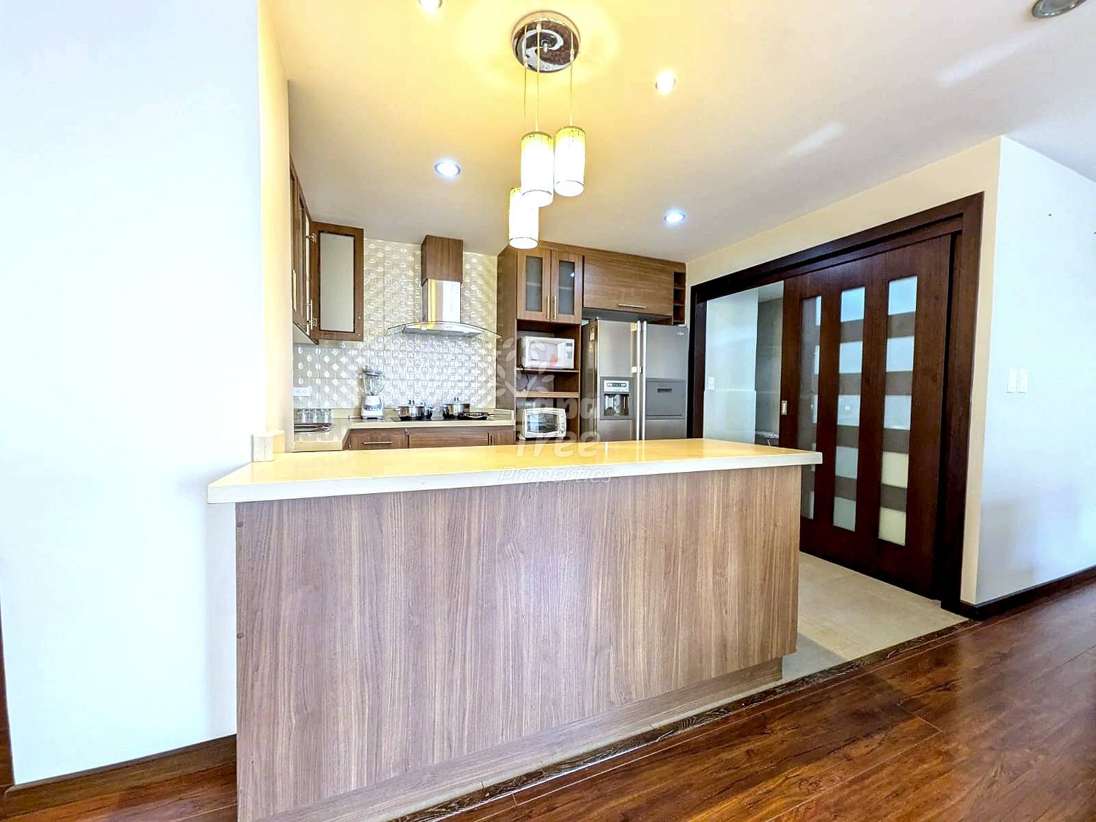 Modern kitchen with wood cabinetry, island counter, stainless steel refrigerator, tile backsplash, pendant lighting, and dark wood glass doors leading to adjacent room.