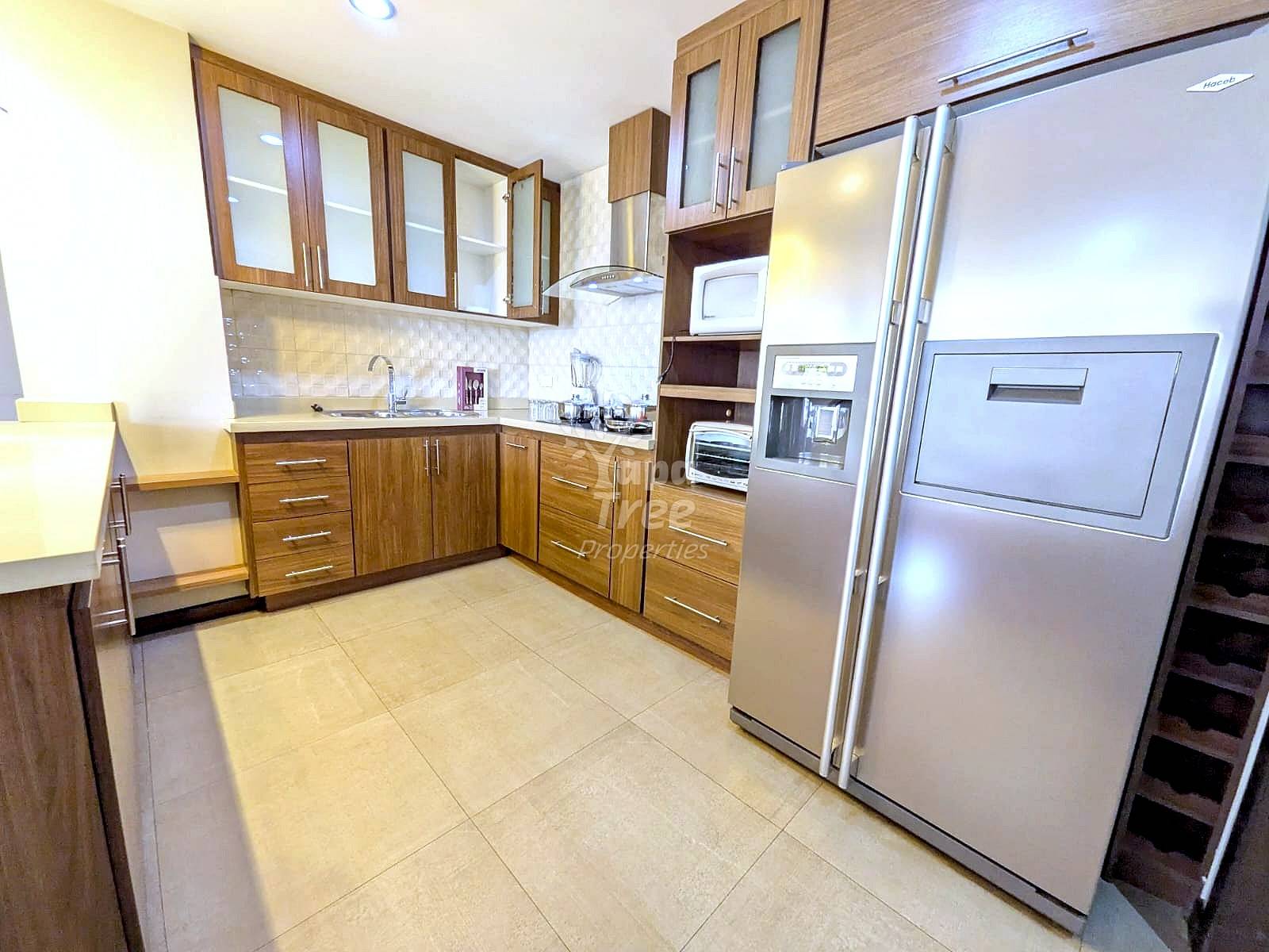 Kitchen with wooden cabinetry, stainless steel refrigerator and range hood, tiled countertop backsplash, and beige tile flooring.