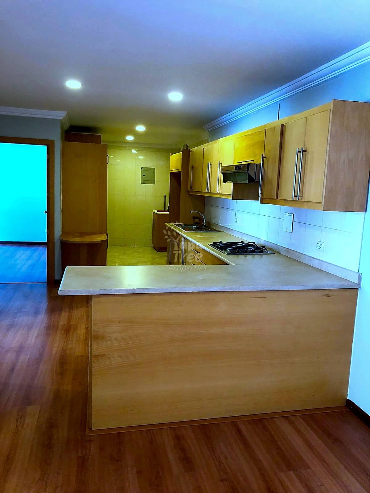 Cocina with wooden cabinetry, gas stovetop, stainless steel appliances, island counter, recessed lighting, and access to adjoining room with hardwood flooring.