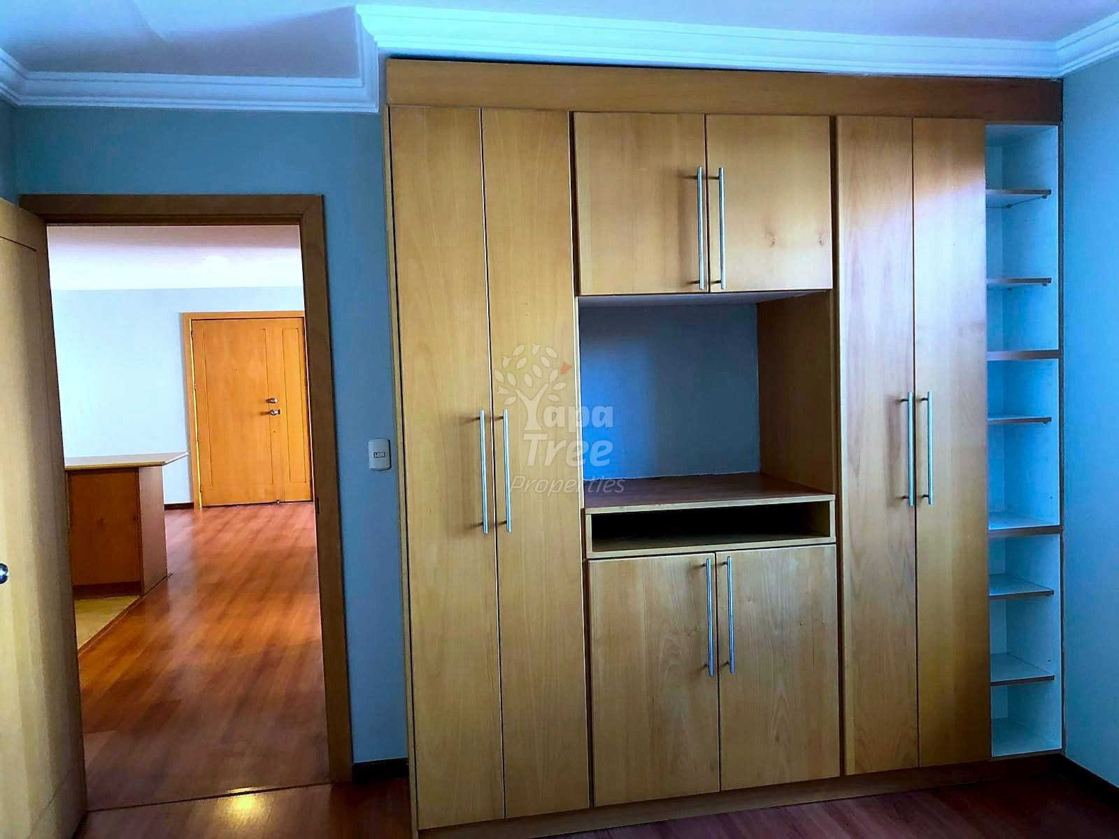 Bedroom with light blue walls, wooden built-in wardrobe with shelving and media display cabinet, hardwood floor, and doorway to adjacent room.